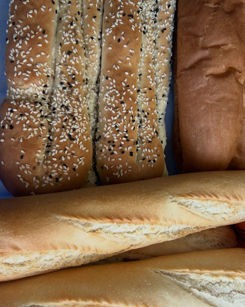 Fresh sesame breadsticks and baguettes stacked close together.
