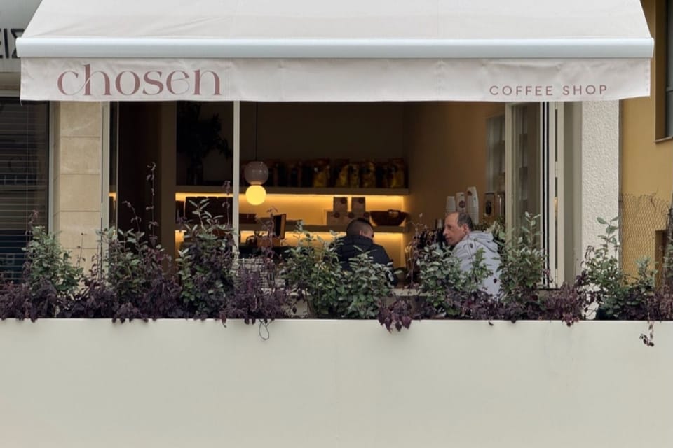 The shop front on Athalassas Avenue: a white awning lettered chosen coffee shop over a planter of dark leaves, with people at the counter inside.